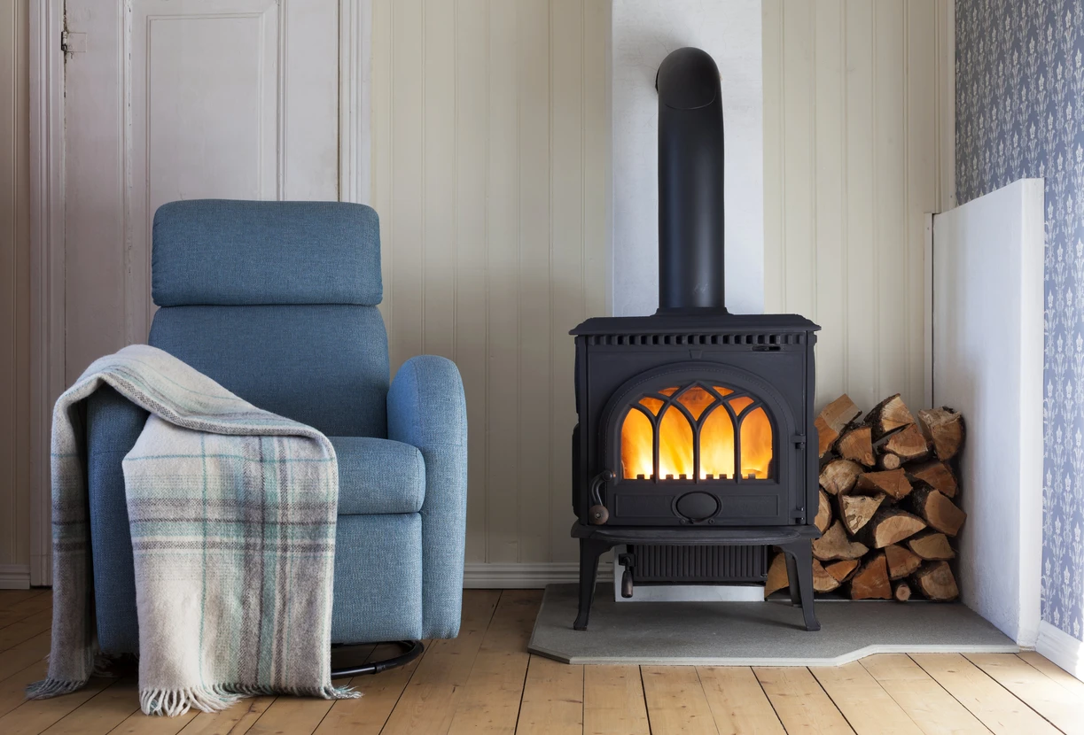 Intérieur chaleureux avec poêle à bois en fonte noire allumé, fauteuil bleu confortable avec plaid écossais, bûches empilées