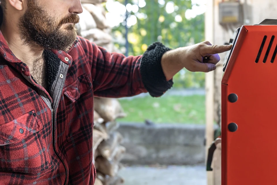 Technicien en combinaison de travail effectuant la maintenance d'une chaudière murale dans une chaufferie domestique